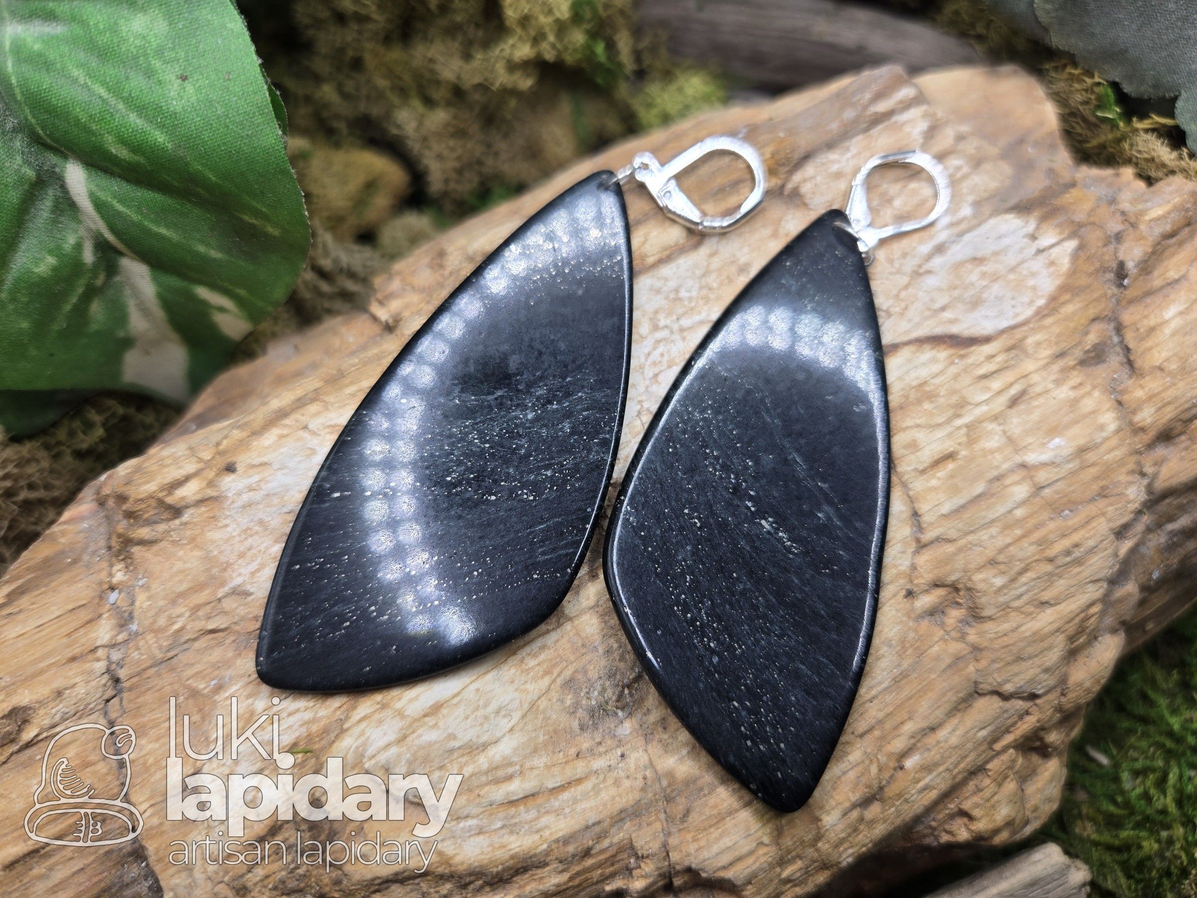 Pair of long black sheen obsidian drop earrings on silver lever-backs, resting on driftwood